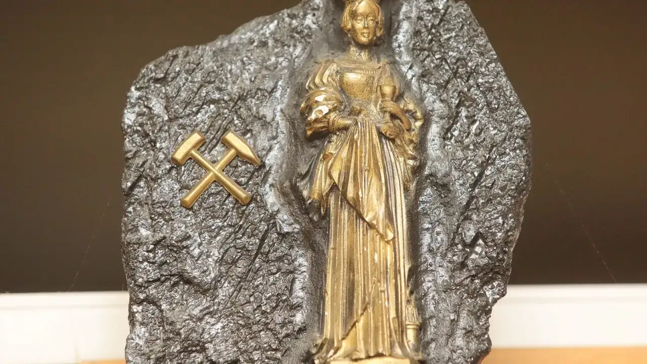 Goldene Figur der Heiligen Barbara, Schutzpatronin der Bergleute, auf einem Felsen mit gekreuzten Schlägeln und Eisen.