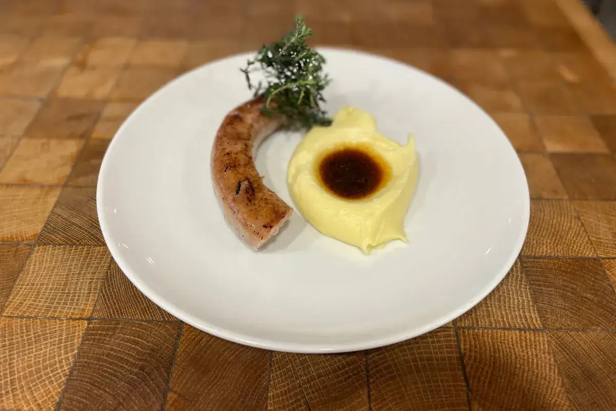 Une saucisse grillée avec une purée onctueuse et sa sauce au centre, garnie de thym frais. Un plat réconfortant de saucisse purée.