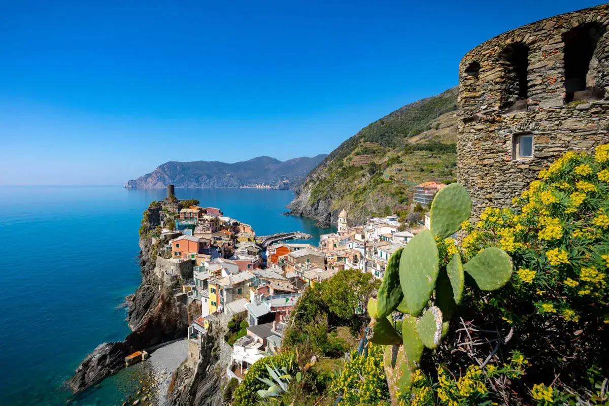 Kolorowe cinque terre miasta, malowniczo położone na klifie nad turkusowym morzem, z kamienną wieżą i kaktusami na pierwszym planie.