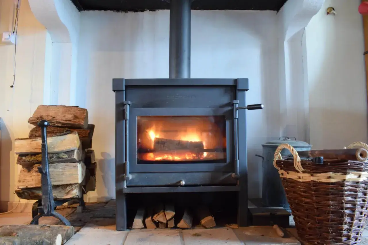 Un poêle à bois avec une sortie façade, prêt à réchauffer la pièce. Des bûches empilées à côté, une ambiance cosy.
