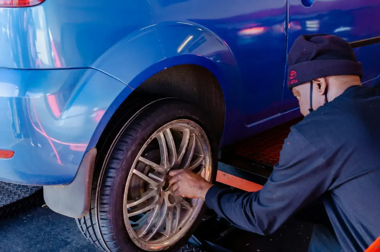 Mężczyzna w czapce z logo Toyoty dokonuje wymiany koła w niebieskim samochodzie.
