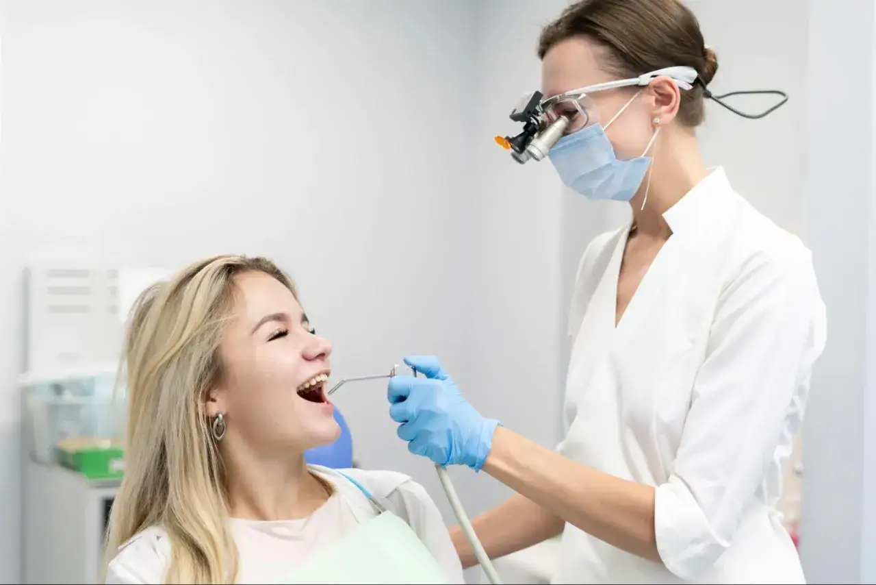 Dentystka w masce i okularach wykonuje piaskowanie zębów w domu pacjentki.