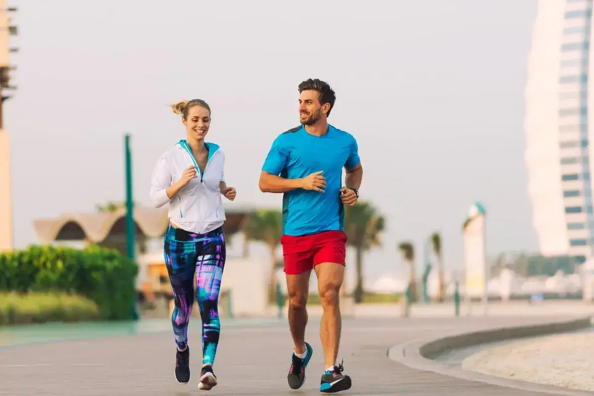 Para biegnie w słońcu. Ona w kolorowych legginsach, on w czerwonych spodenkach. Cieszą się wspólnym, spokojnym **slow joggingiem** wzdłuż plaży.