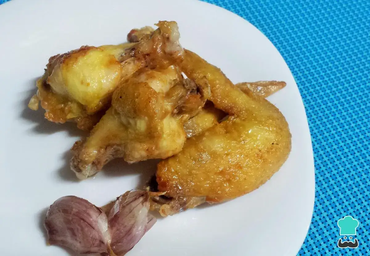 Alitas de pollo al ajillo doradas y jugosas, servidas en un plato blanco con un diente de ajo.