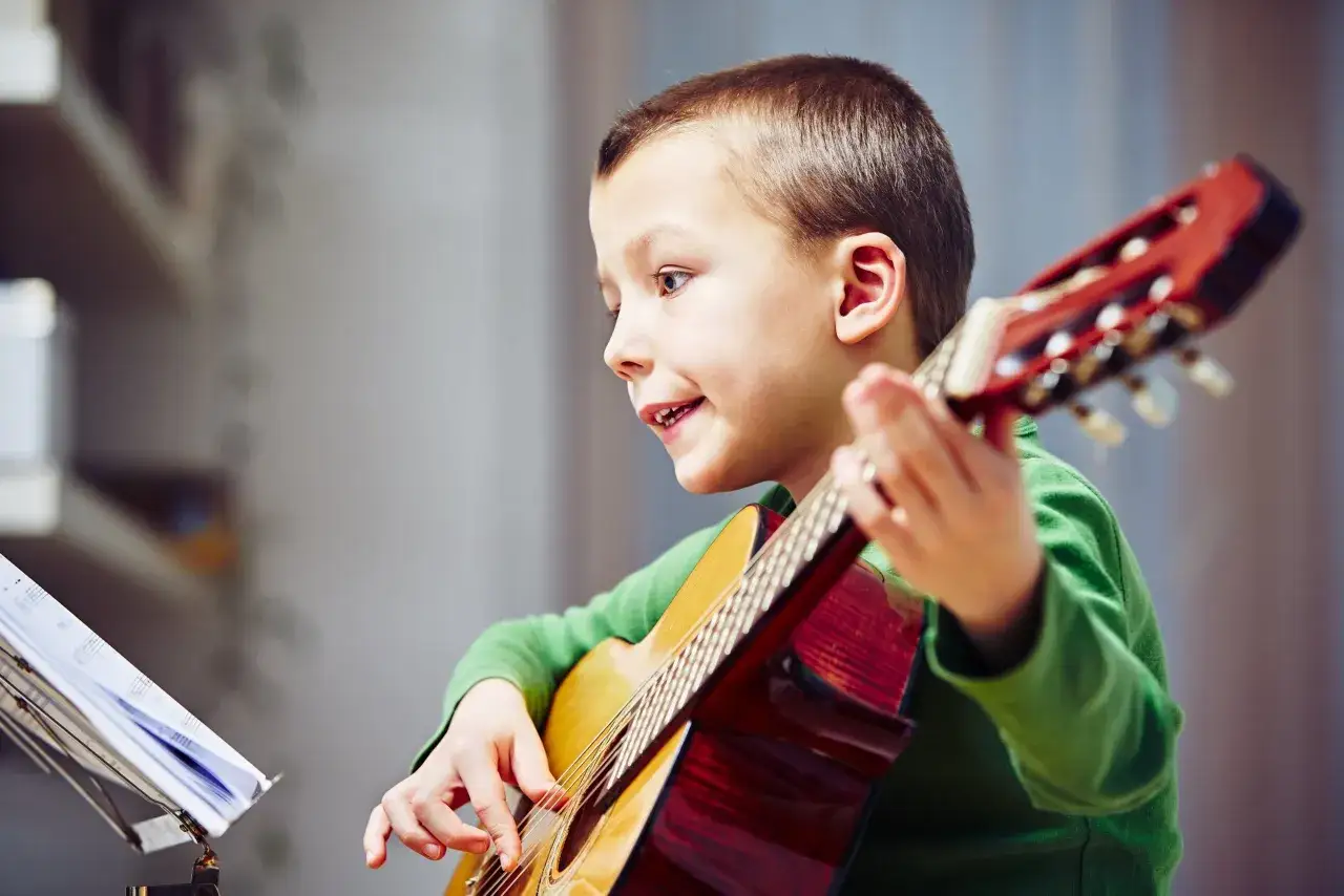 Chłopiec w zielonej bluzce z zapałem gra na gitarze, patrząc na nuty.