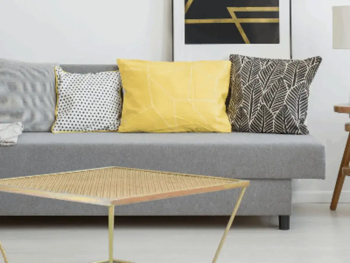 Sofa z poduszkami: szara, żółta z geometrycznym wzorem, czarno-biała w liście. Kolor żółty znaczenie: radość i optymizm.