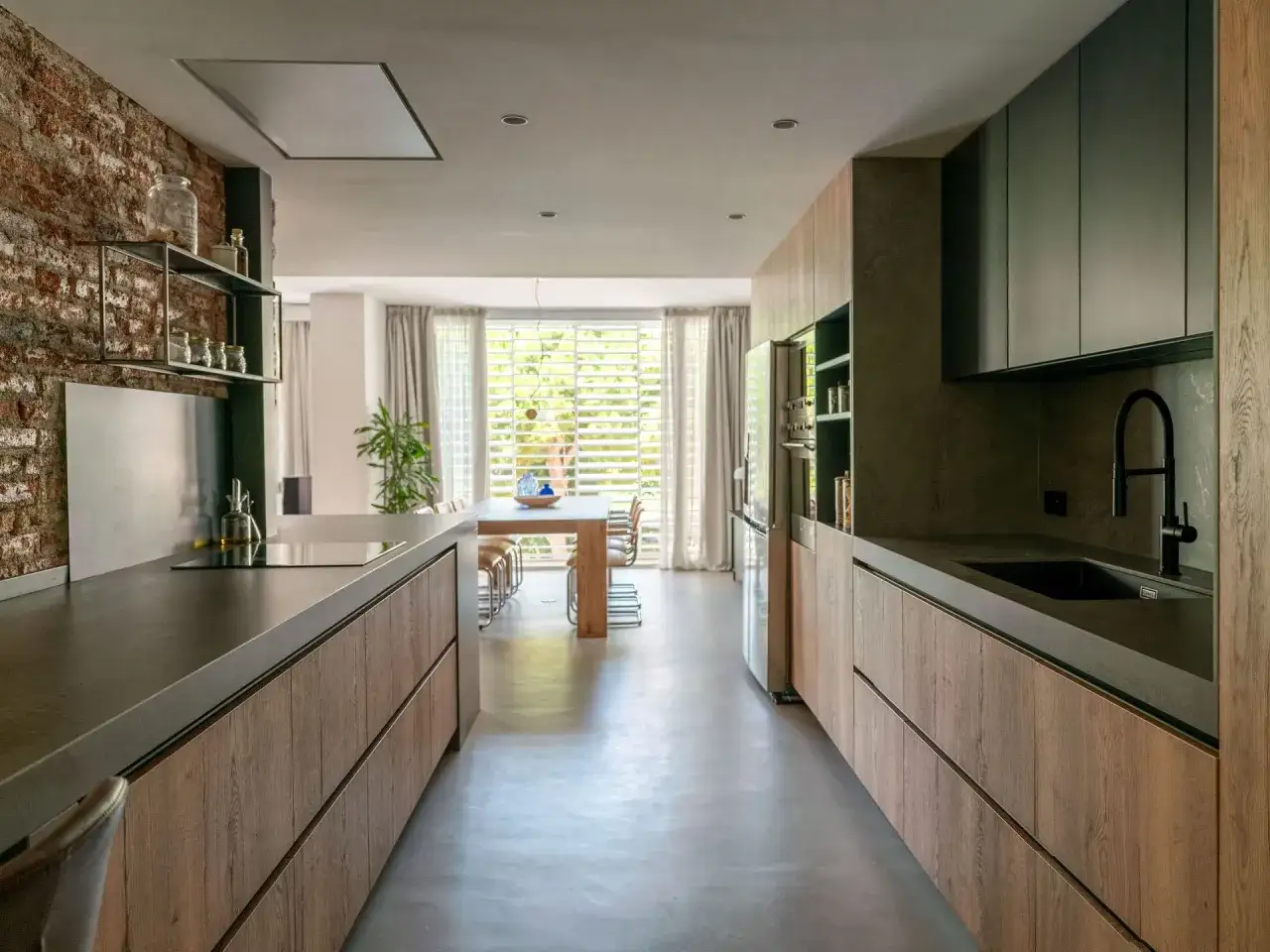 Cocina alargada con encimeras de hormigón y armarios de madera. Una isla central divide el espacio, ideal para saber cómo distribuir una cocina alargada.