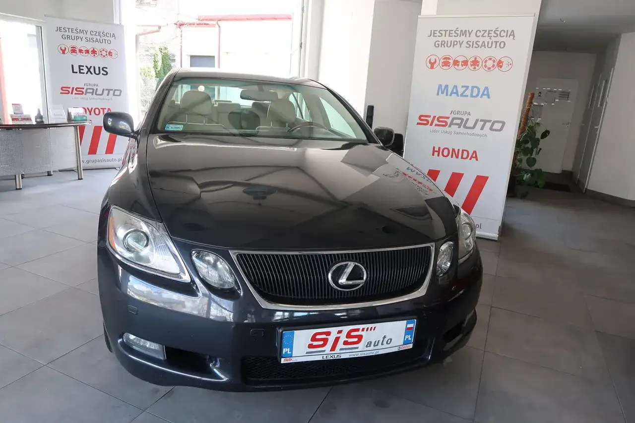 Ciemnoszary Lexus GS w salonie, gotowy na relaks. Obok banery grup SISAUTO z markami Mazda i Honda.