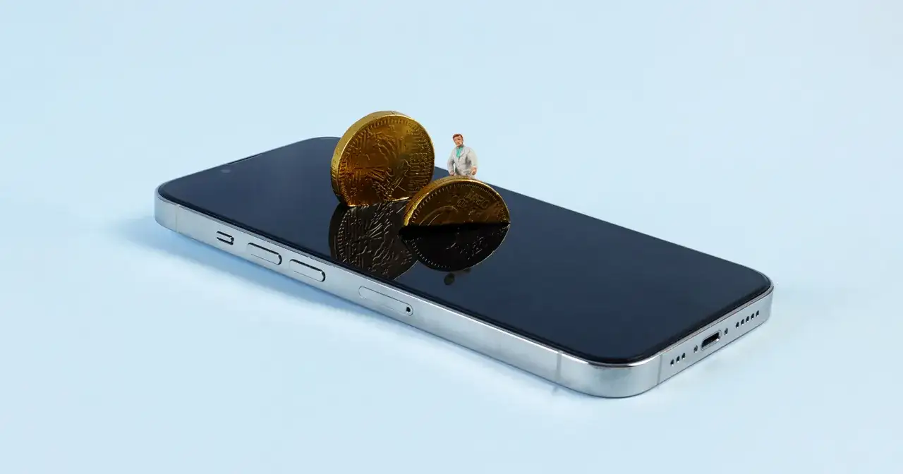 Un hombrecito observa dos monedas de chocolate sobre un teléfono, como si fuera un wallet que es.
