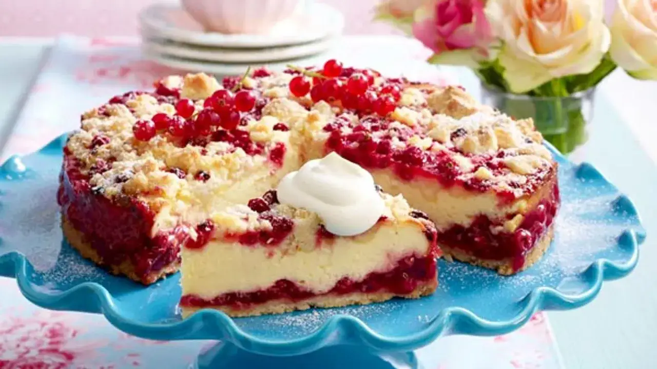 Saftiger Johannisbeerkuchen mit Quark und Streuseln, garniert mit frischen roten Johannisbeeren und einem Klecks Sahne.