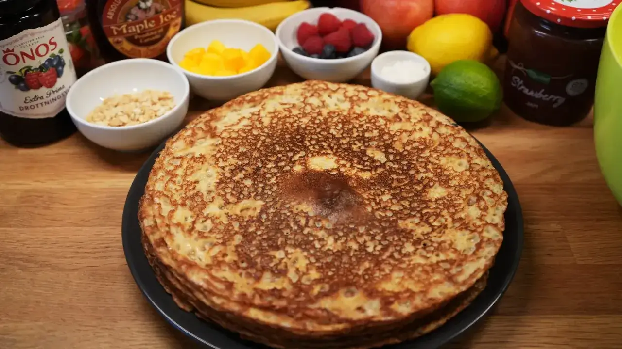 En hög med gyllene pannkakor, redo för servering med sylt, frukt och nötter. Ett perfekt pannkakor recept för en mysig frukost eller fika.
