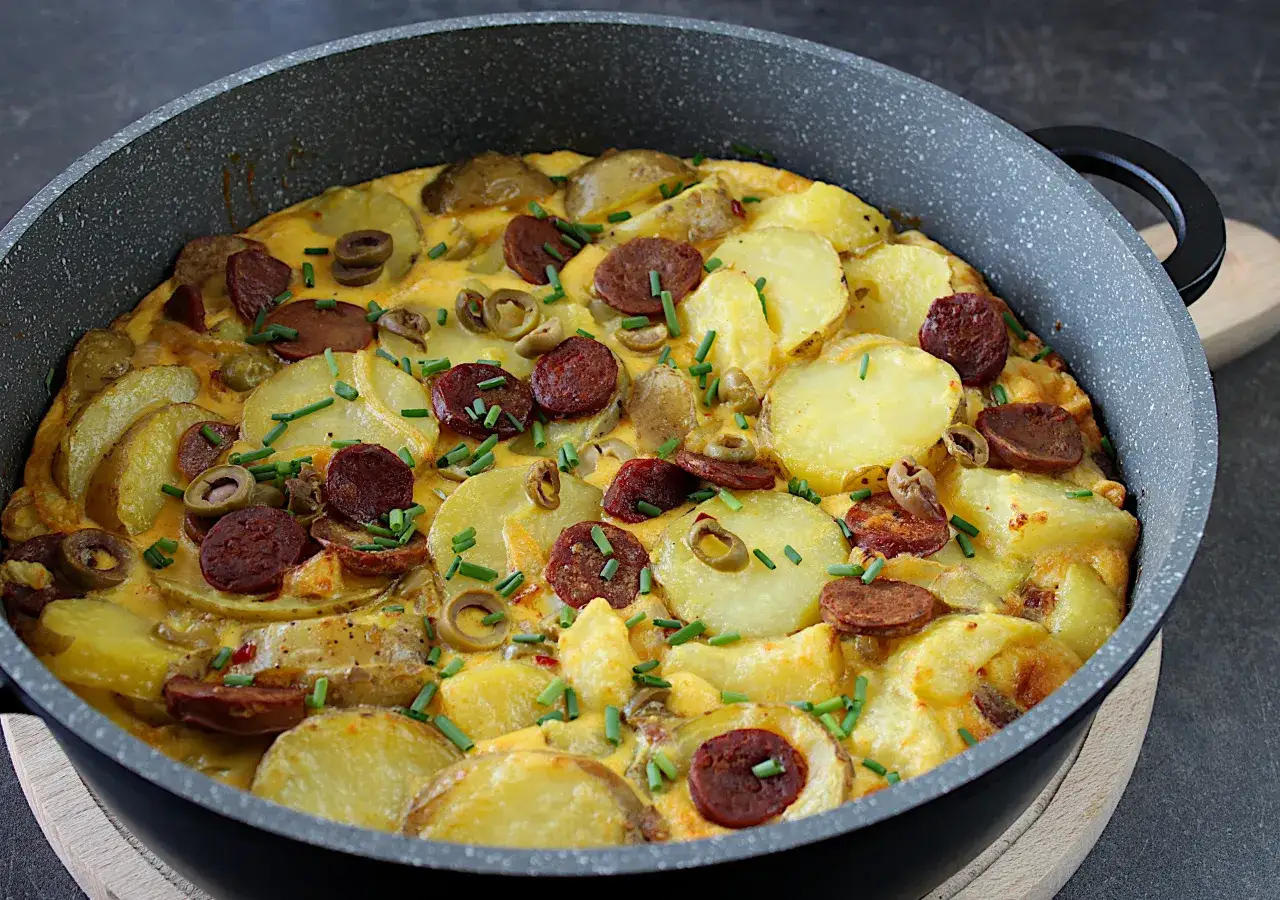 Pyszna tortilla de patatas z ziemniakami, chorizo i oliwkami, posypana szczypiorkiem, prosto z patelni.