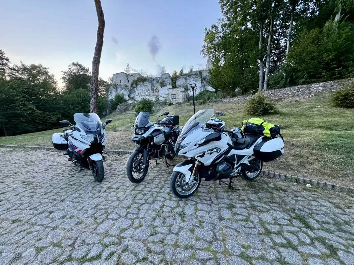 Trzy motocykle BMW gotowe na odkrywanie tras motocyklowych Śląsk. W tle ruiny zamku i zielone drzewa.