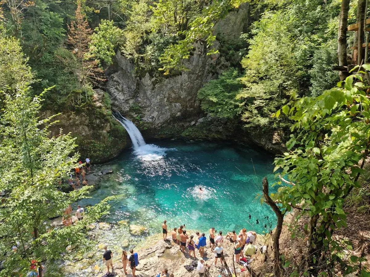 Türkisblaue Lagune mit Wasserfall in Albanien, Theth. Menschen genießen das kühle Wasser inmitten üppiger Natur.