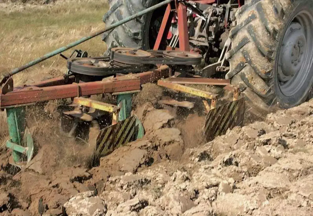 Część pługa pracującego w polu, odwracająca ziemię. Widać koła ciągnika i mechanizm roboczy.