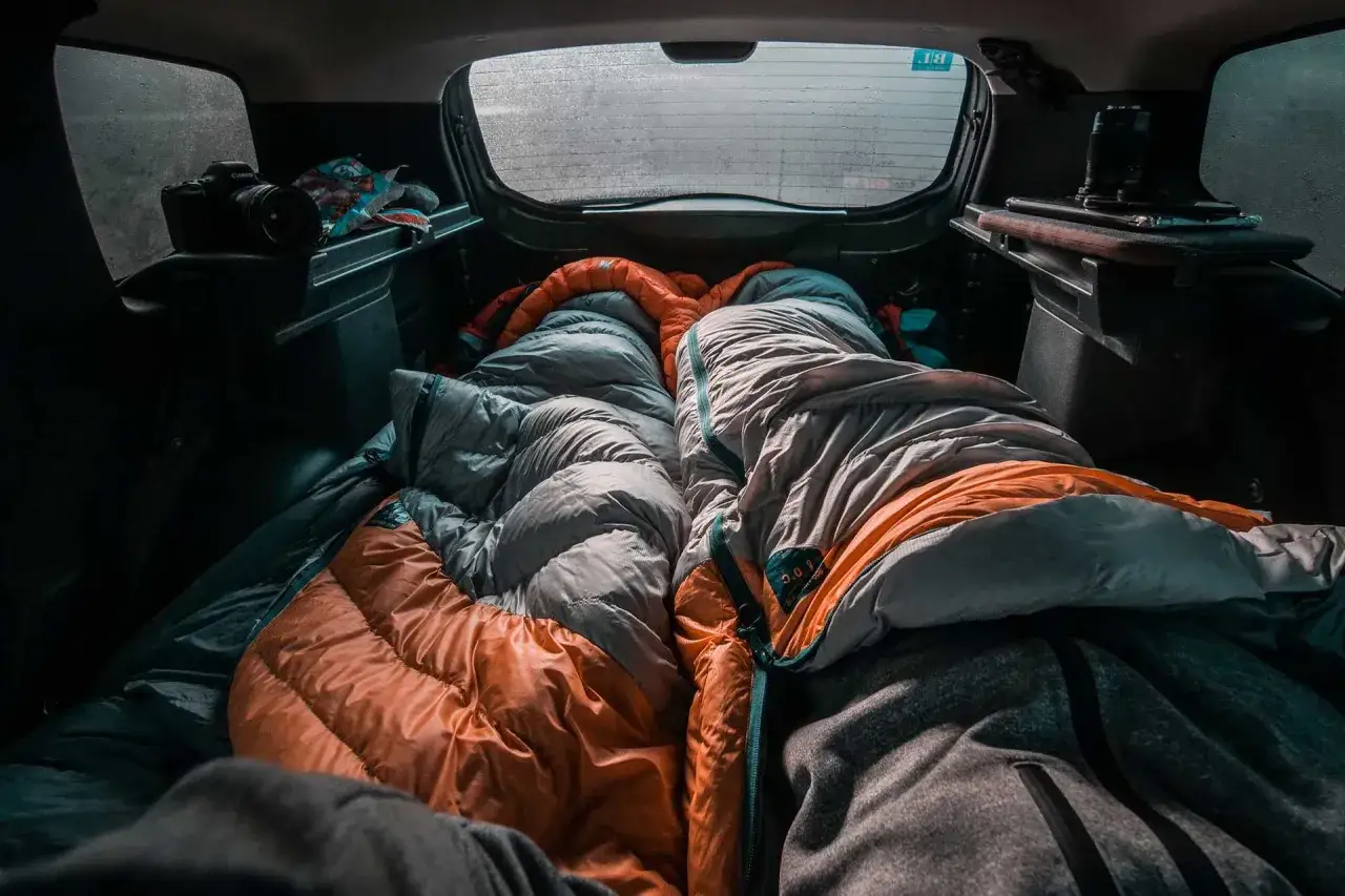 Gemütlich schlafen im Auto, zwei Schlafsäcke liegen bereit. Eine Kamera und Snacks sind auch da für das Abenteuer.