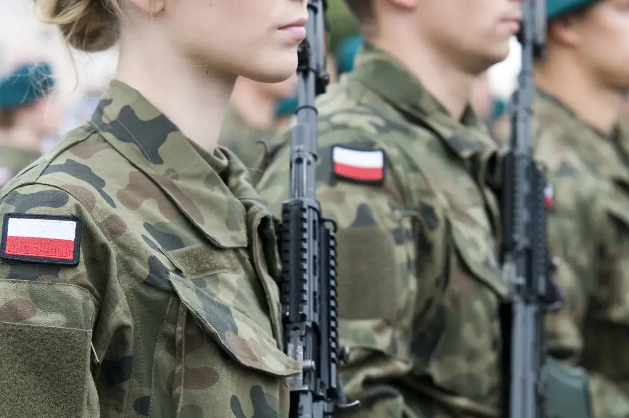 Żołnierze w mundurach z polskimi flagami, gotowi do marszu. Słychać przyśpiewki wojskowe do marszu.