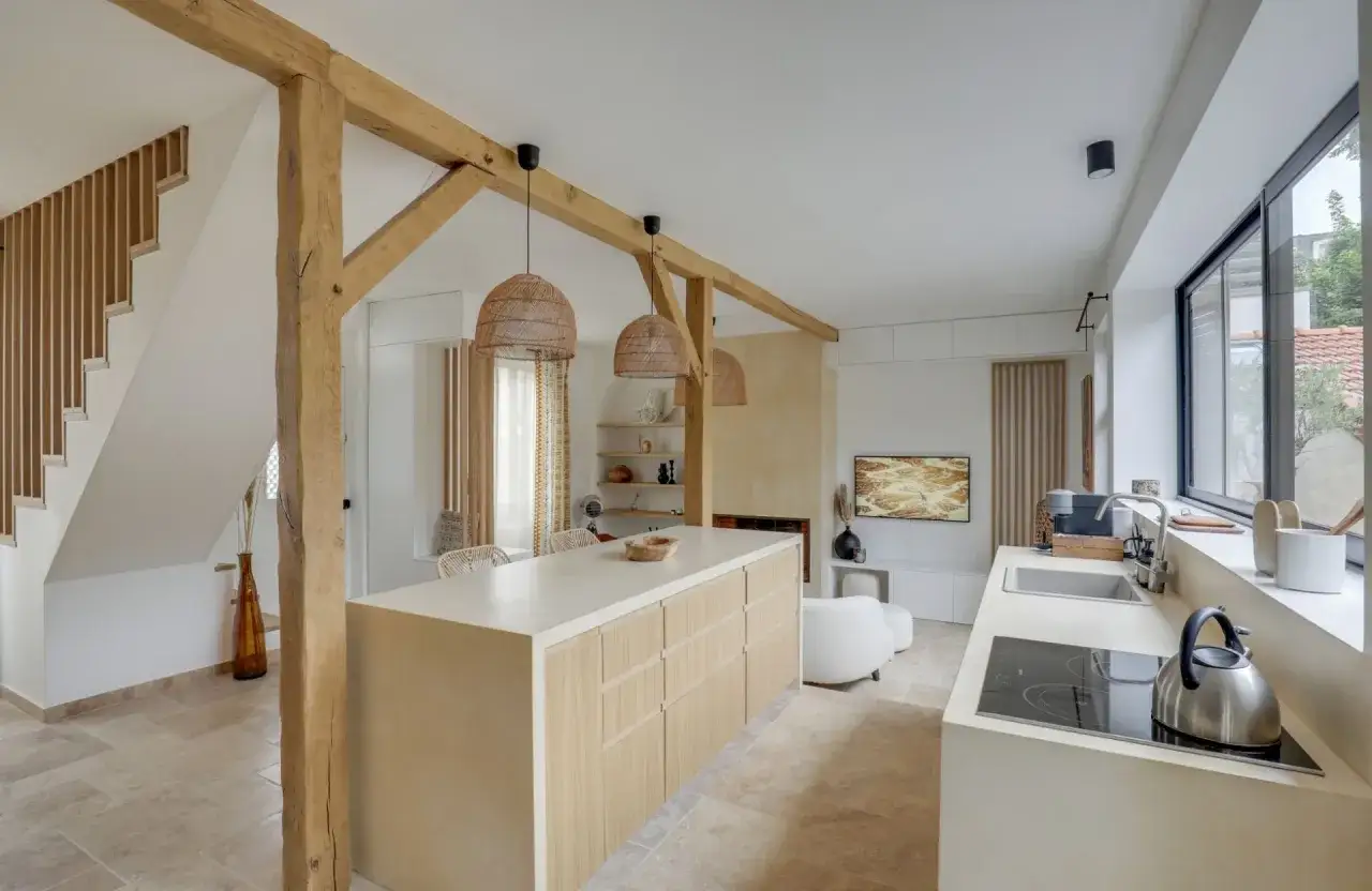 Plan d'une cuisine en longueur avec &icirc;lot central en bois clair, poutres apparentes, et un coin salon TV.