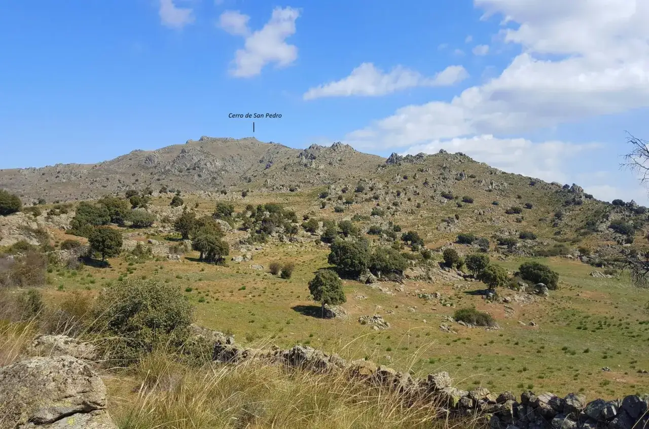 Paisaje rocoso y verde con el **cerro de San Pedro** en Colmenar Viejo al fondo.