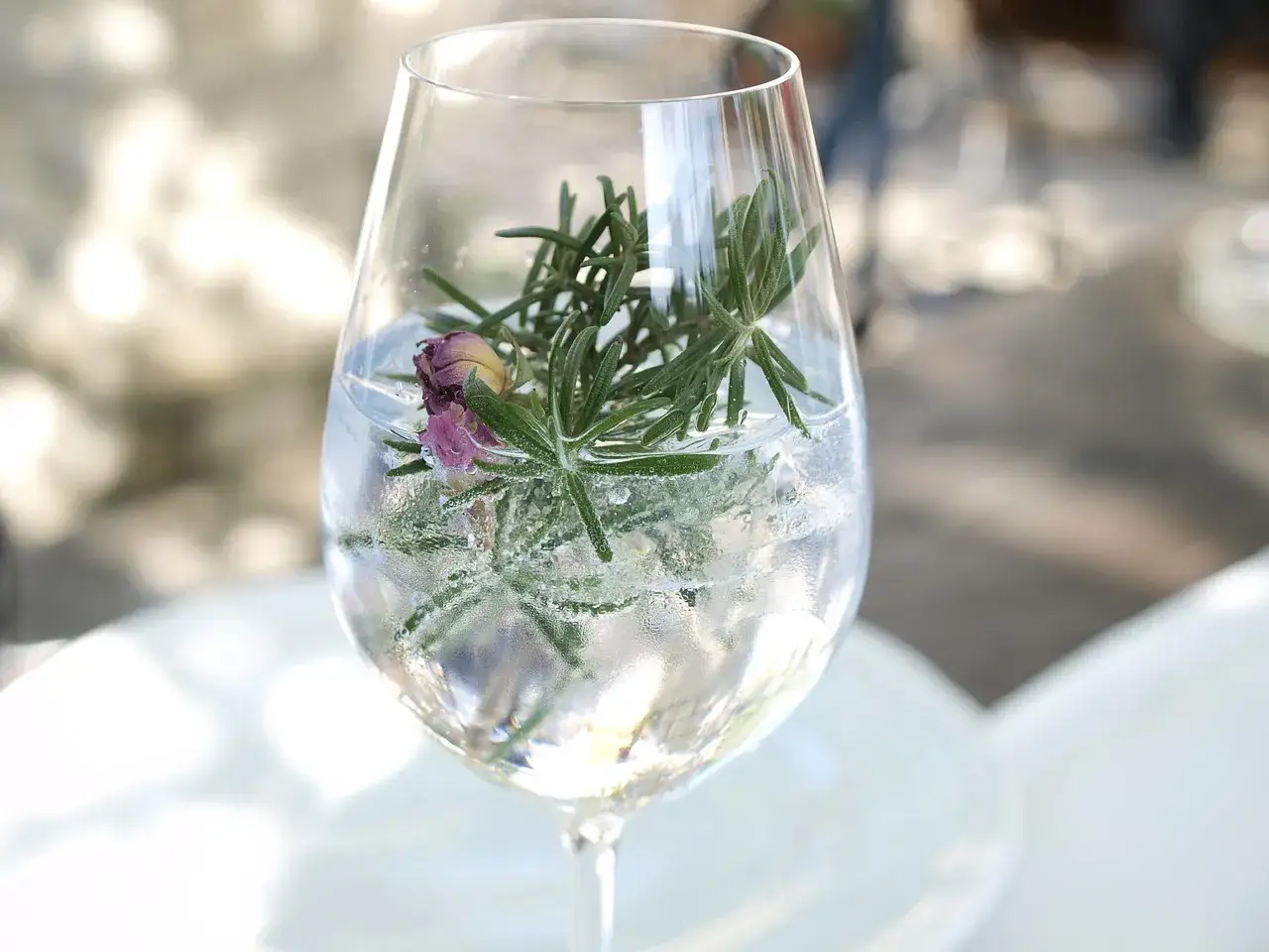 Elegancki aperitif w kieliszku z rozmarynem i pączkiem róży. Orzeźwiający napój na letnie popołudnie.