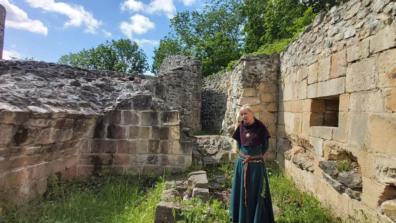Kobieta w stroju historycznym stoi wśród ruin najstarszego zamku w Polsce.
