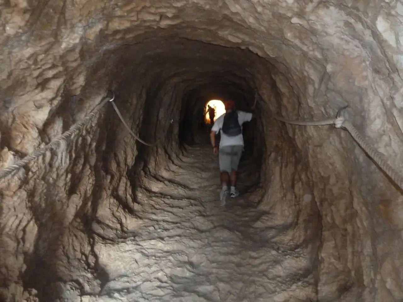 Hombre camina por t&uacute;nel rocoso con cuerdas de seguridad, parte del sendero del Pe&ntilde;&oacute;n de Calpe.