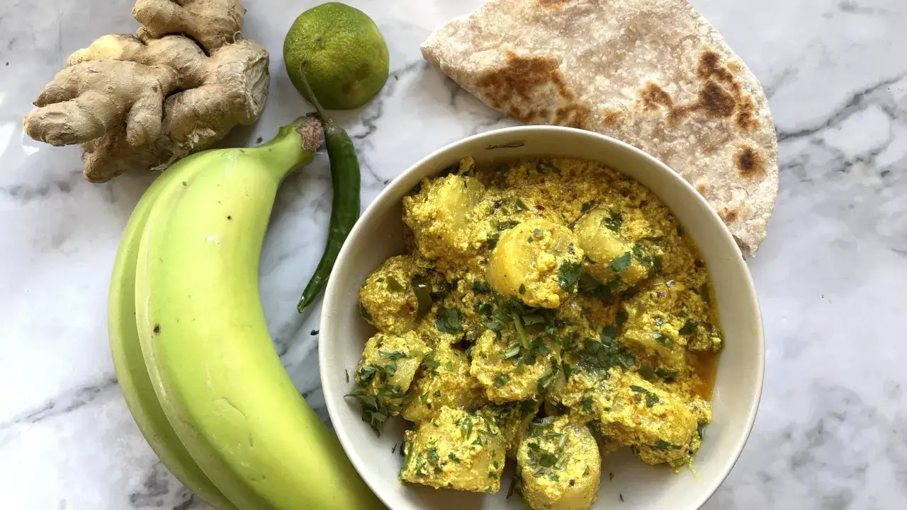 Ein cremiges Bananencurry mit Koriander, serviert mit Fladenbrot, gr&uuml;nen Bananen, Ingwer, Limette und Chili.