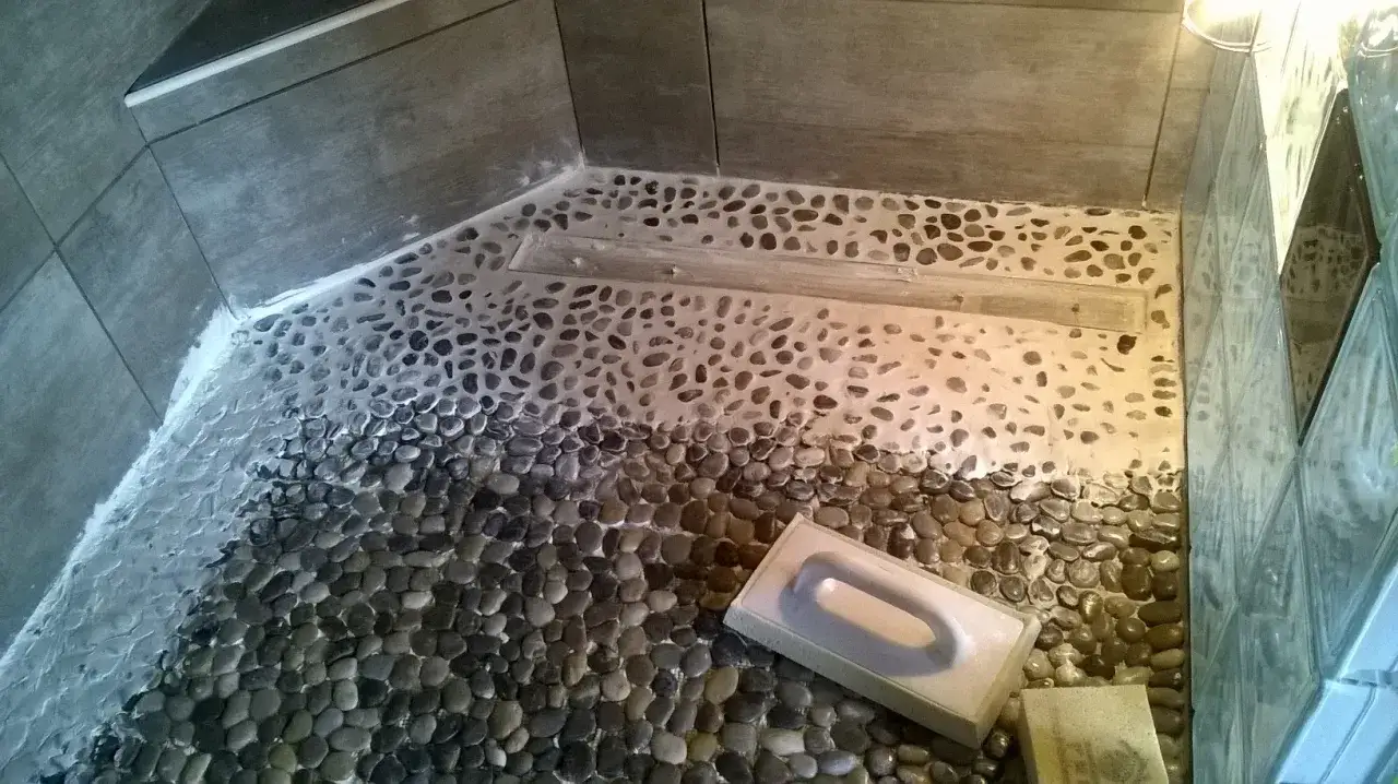 Application d'un joint &eacute;poxy sur un sol de douche en galets. Un outil blanc est pos&eacute; sur les galets.