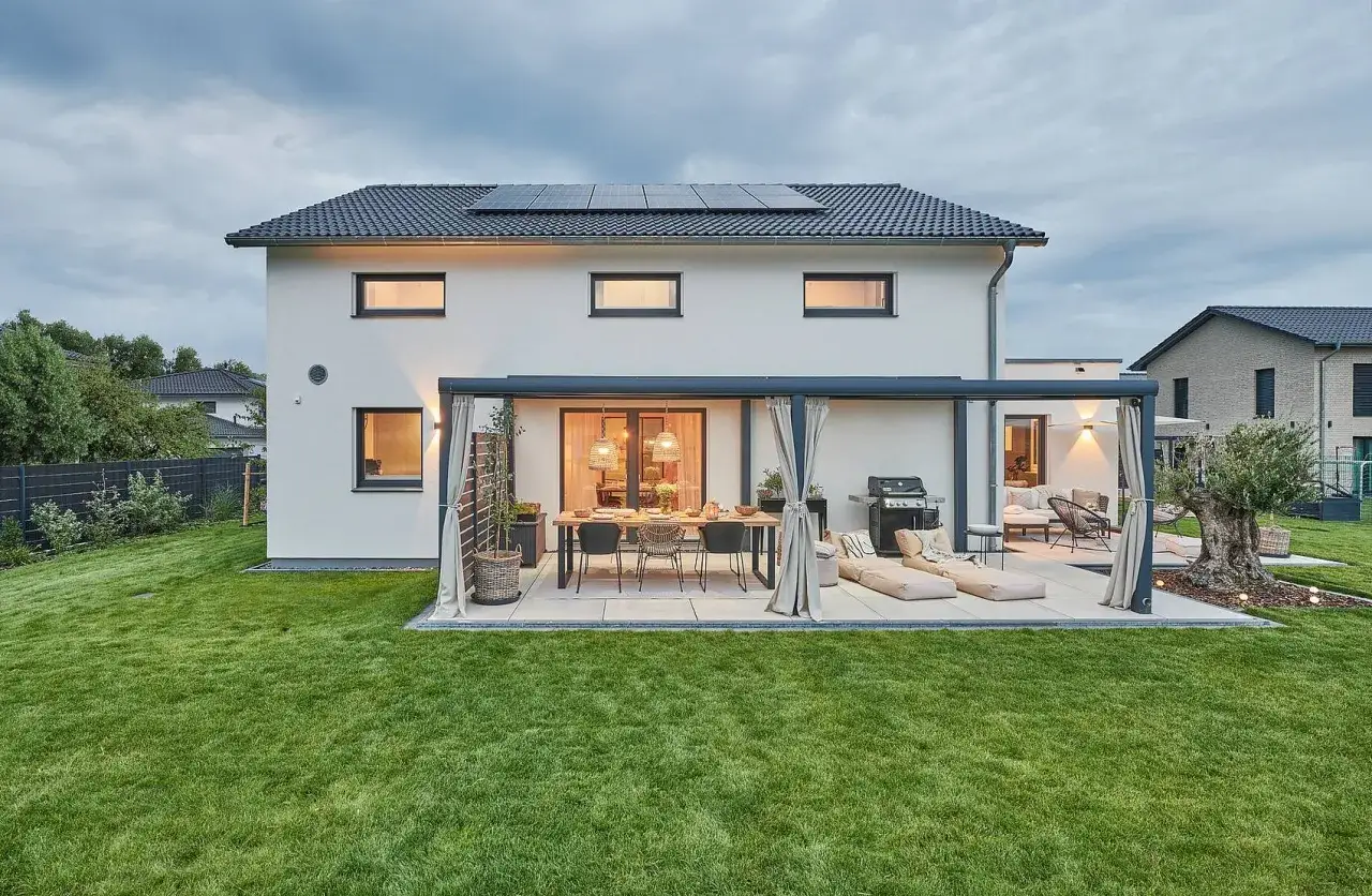 Moderne Terrasse mit Essbereich und Lounge-M&ouml;beln, &uuml;berdacht von einer Pergola. Ein Grill steht bereit. Der **Erker im Erdgeschoss** des Hauses ist gut integriert.