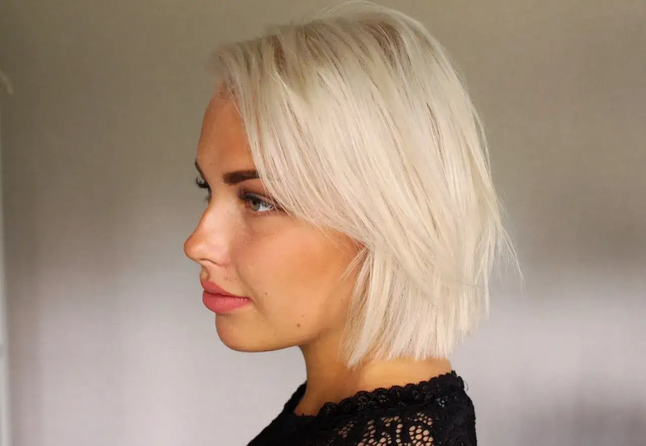 Profilbild på en kvinna med blont hår och ljus hy. Hennes ögon är gröna och hon har rosa läppar. Håret är kortklippt och stylat med en sidbena. Hon bär en svart spetsklänning. Det finns fyra anledningar till att hennes hår ser ut som frusen sand.
