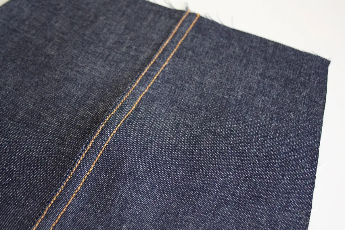 Close-up of dark denim fabric with a double orange stitch, perfect for a jeans sewing pattern free project.