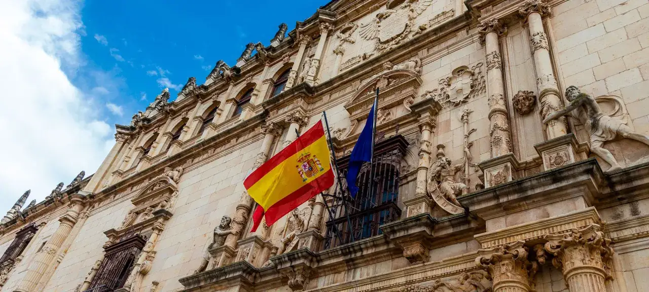 Majestatyczny budynek w Alcalá de Henares z hiszpańską flagą powiewającą na wietrze.