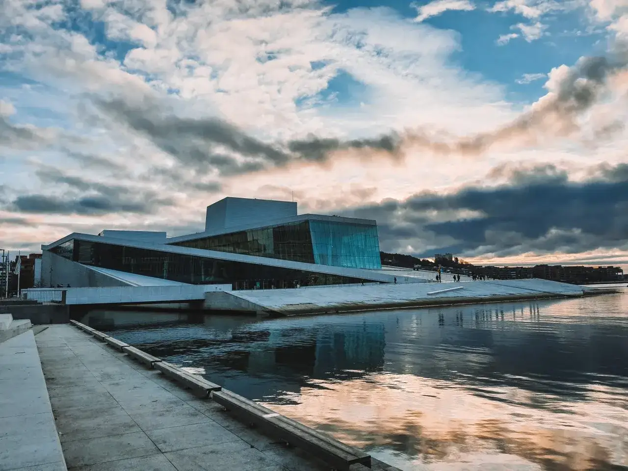 Oslo na weekend: nowoczesna Opera z lodową fasadą odbija się w wodzie przy pochmurnym niebie. Idealne miejsce na spacer.