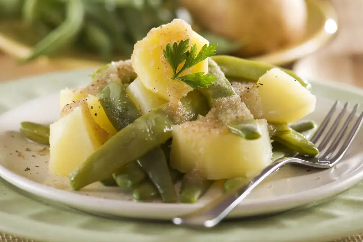 Fagiolini bolliti e patate conditi con erbe aromatiche e pangrattato, serviti su un piatto bianco.