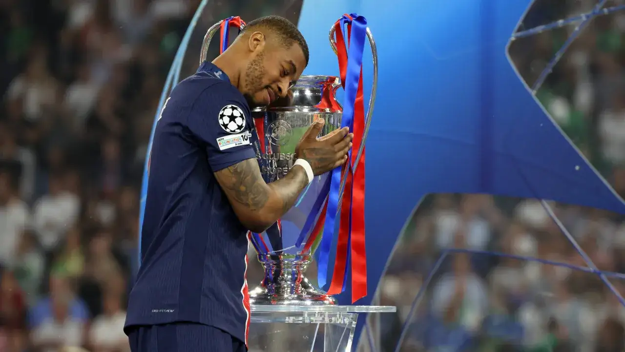 Piłkarz Kimpembe przytula Puchar Ligi Mistrzów, wyrażając radość i dumę z osiągnięcia.