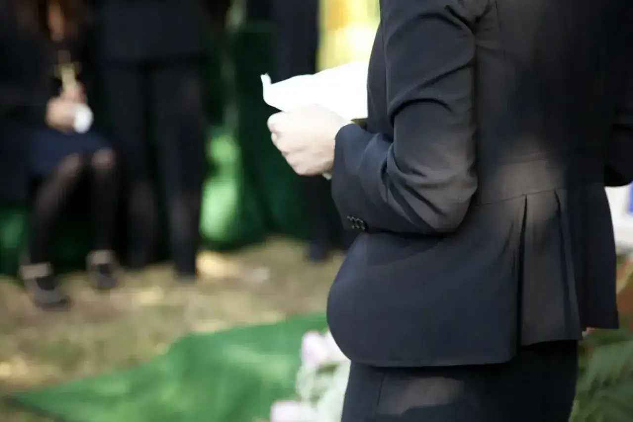 Smutne wspomnienie o zmarłej osobie. Kobieta w czerni trzyma kartkę, być może przemówienie pożegnalne.