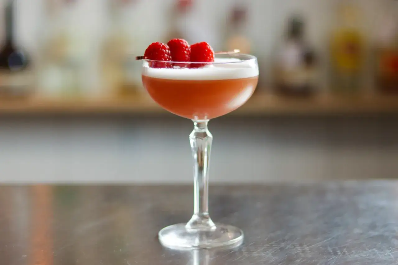En elegant french martini med kr&auml;mig skum och tre hallon p&aring; en cocktailpinne, redo att avnjutas.