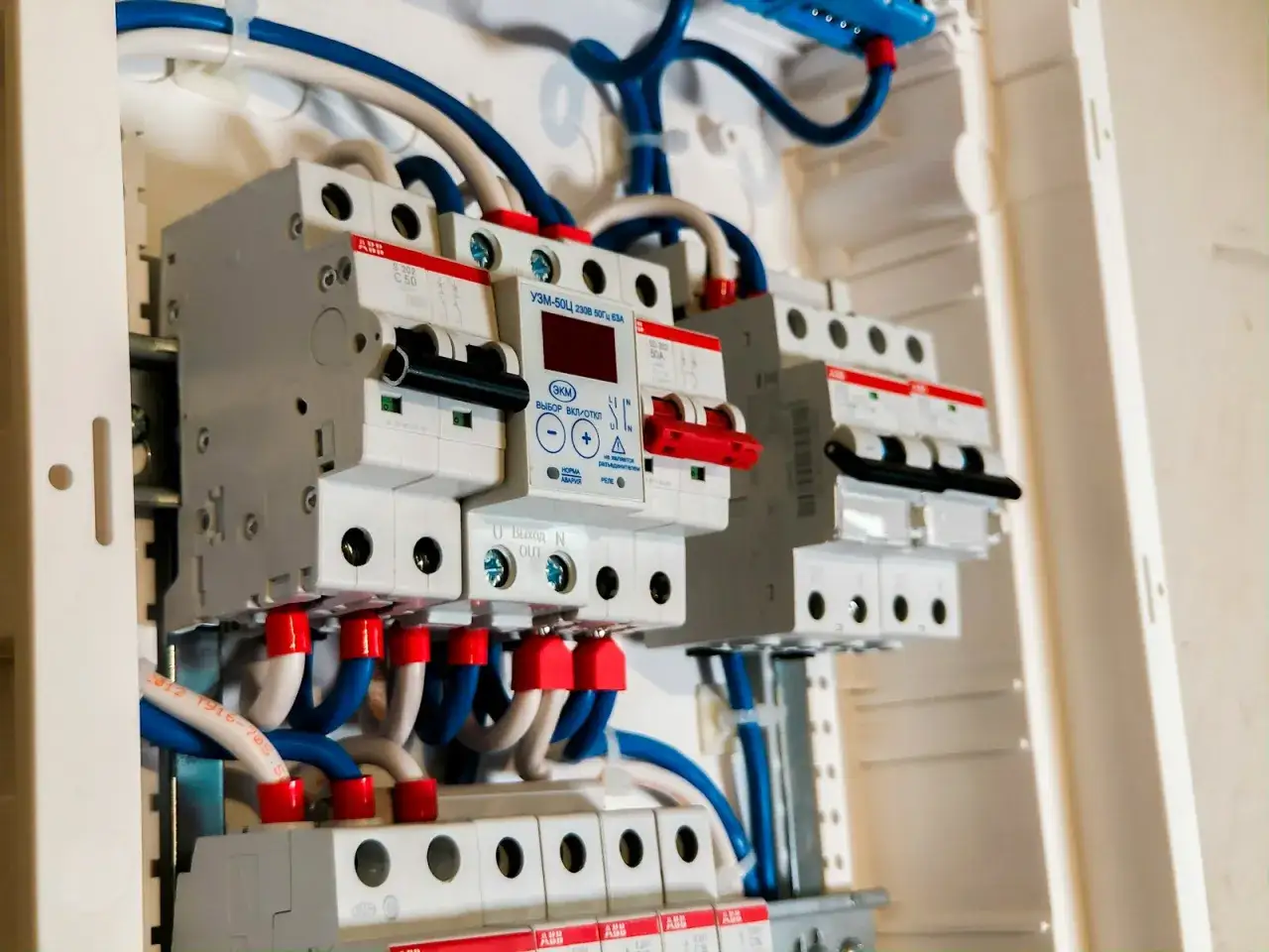 Wewnątrz białej obudowy widać prosta instalacja elektryczna z wyłącznikami, przewodami i cyfrowym modułem sterującym.