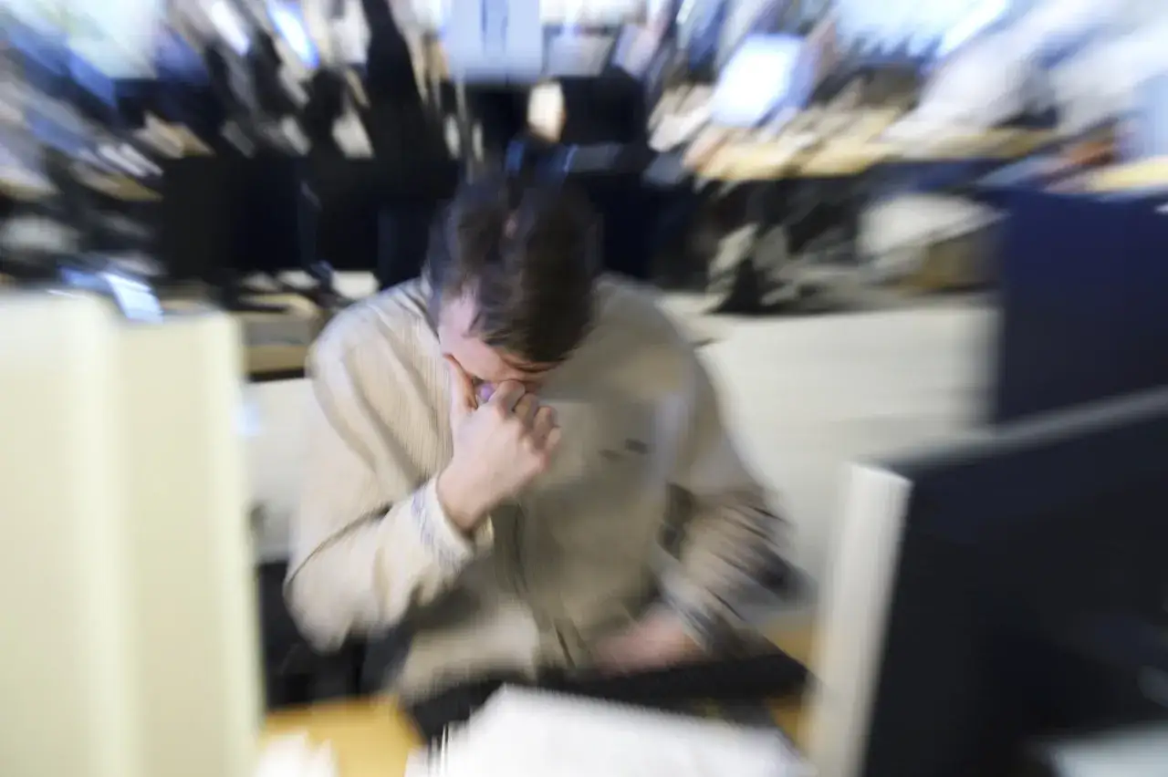 En person sitter vid ett skrivbord, gnuggar sig i ögonen och ser ut att ha det jobbigt. Känns som att jag hatar mitt jobb.