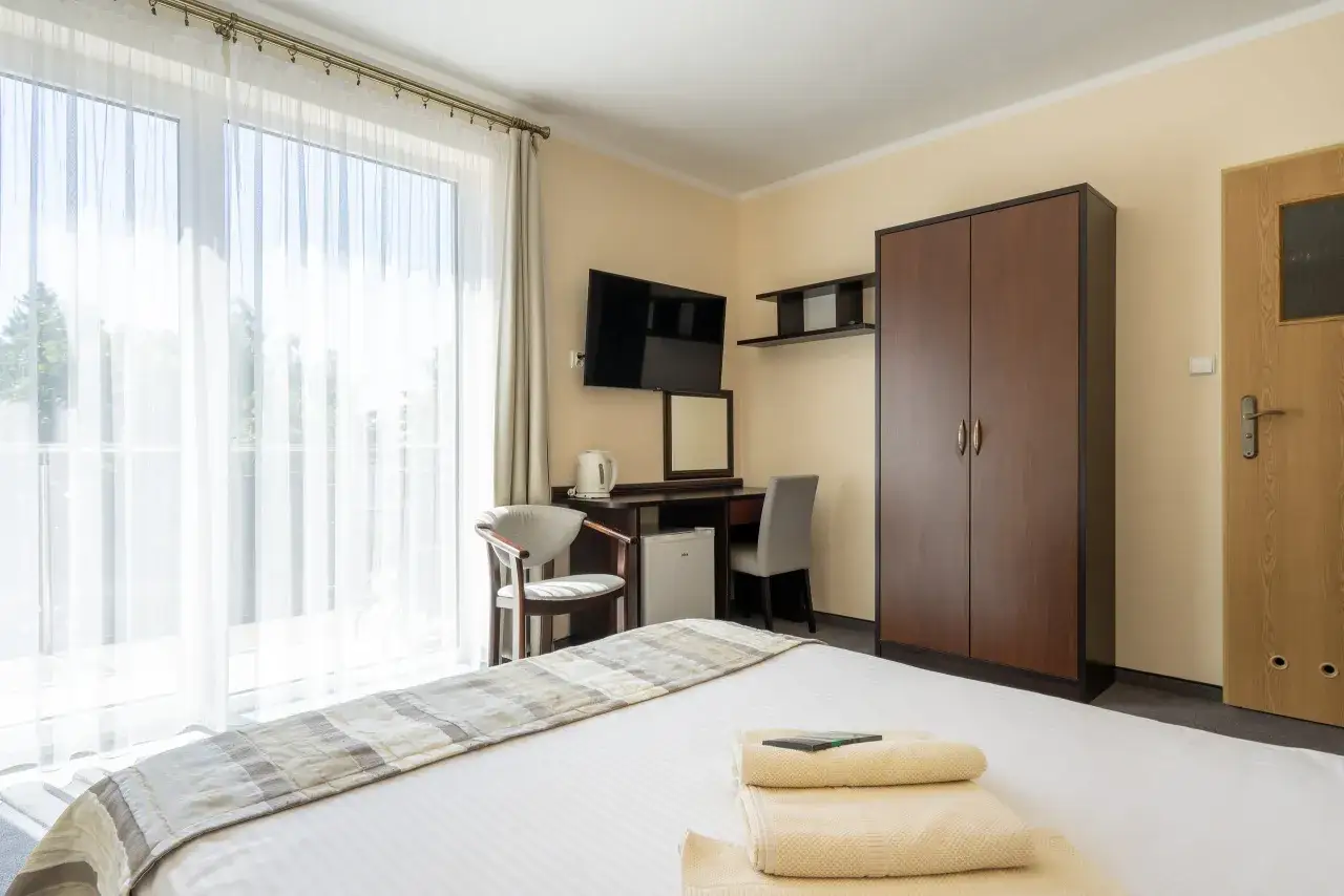 Pokój w pensjonacie Pirat Jastrzębia Góra: łóżko, szafa, biurko z lustrem, czajnik, lodówka, TV i balkon.