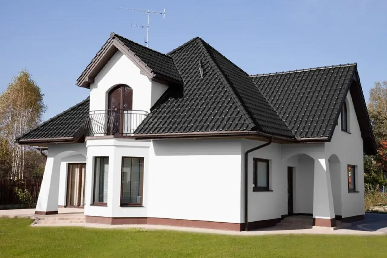 Biały dom z ciemnym dachem. Czy to kolor ral 7016? Elegancka biel ścian kontrastuje z grafitową dachówką.