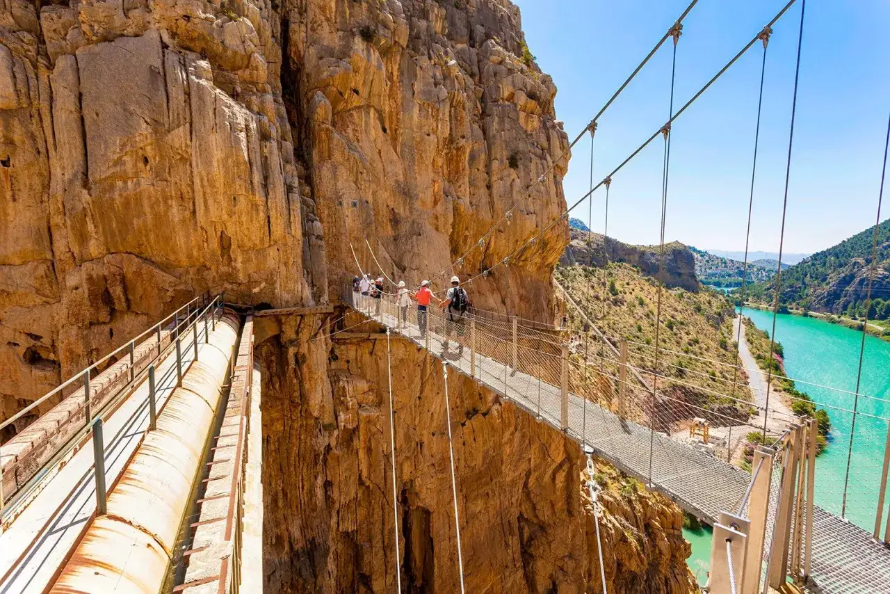 Menschen genie&szlig;en das Malaga Wandern auf einer H&auml;ngebr&uuml;cke &uuml;ber einer Schlucht mit t&uuml;rkisfarbenem Wasser.