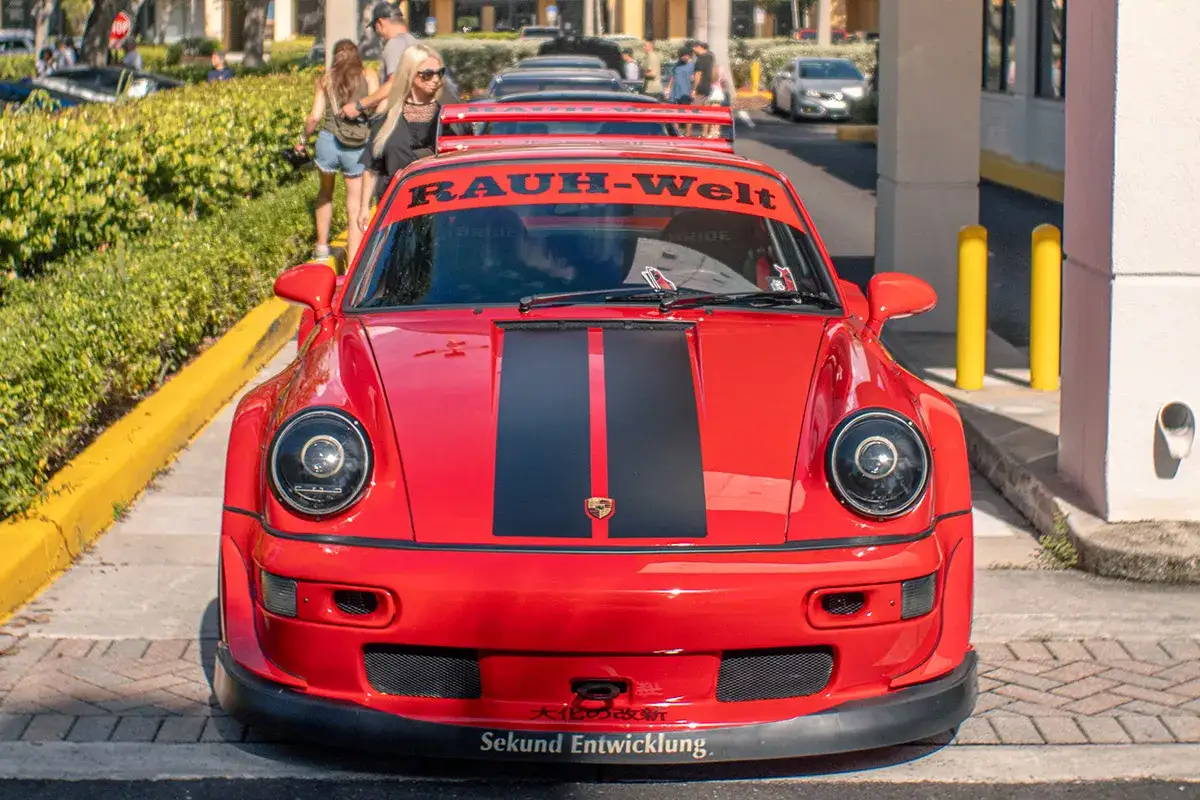 Czerwone Porsche RWB z czarnymi pasami na masce i spojlerem. Na przedniej szybie napis
