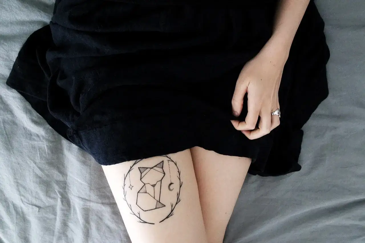 Tatuaż lisa w stylu origami na udzie, otoczony gałązkami. Wygląda jakby przetrwał próbę czasu, niczym tatuaż po 30 latach.