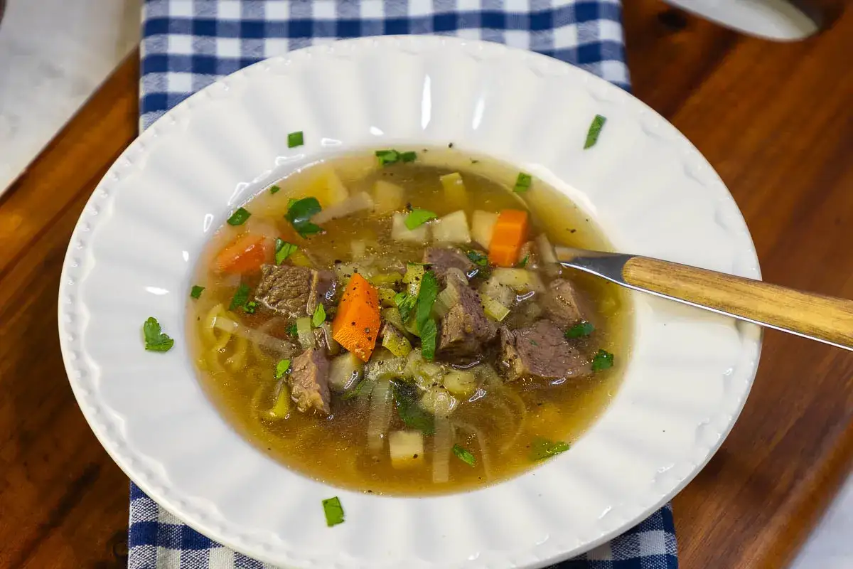 Eine dampfende Sch&uuml;ssel mit Omas frischer Suppe, gef&uuml;llt mit zarten Fleischst&uuml;cken, Karotten, Kartoffeln und Kr&auml;utern.