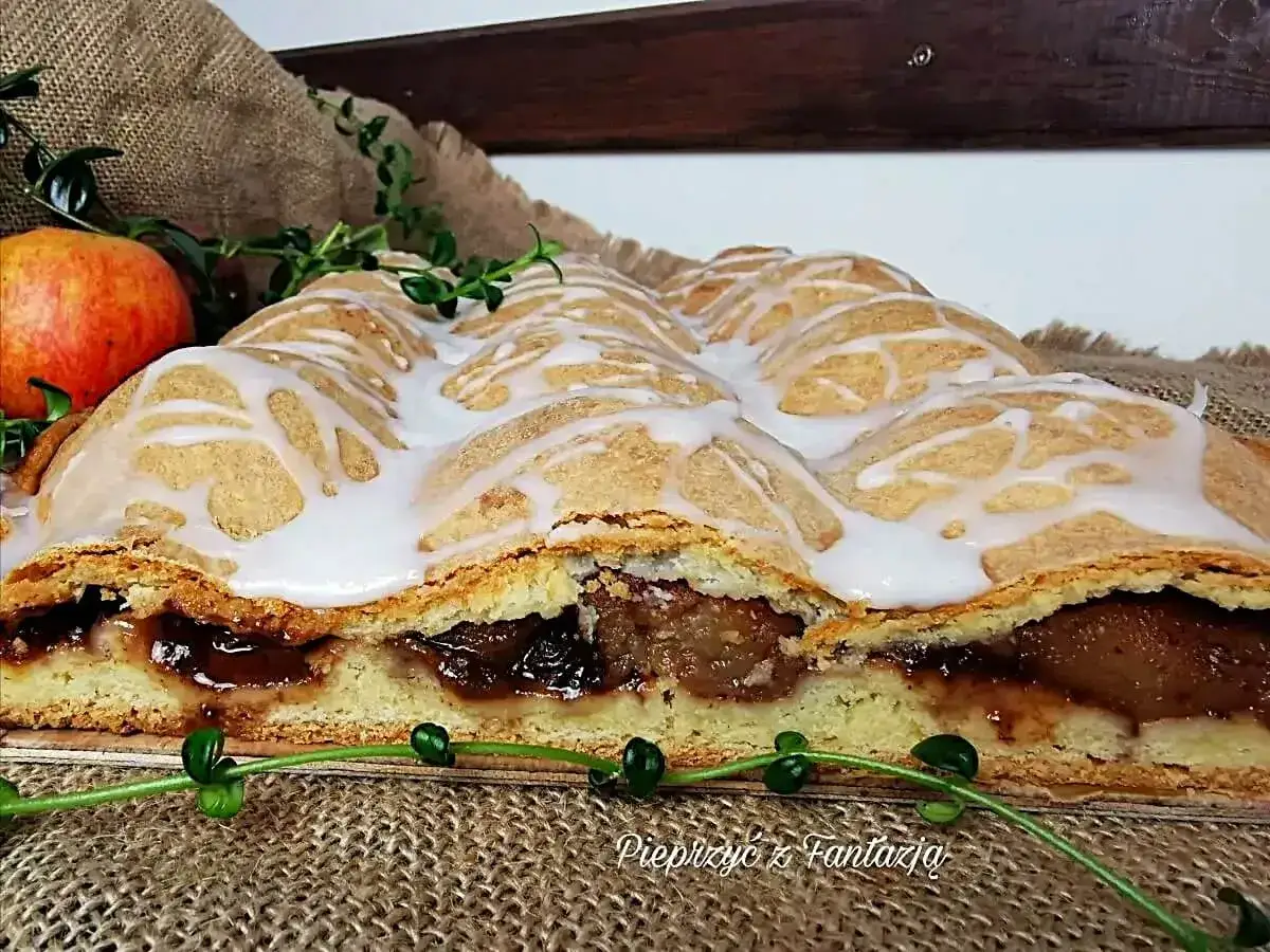 Szybkie łatwe ciasto z powidłami, udekorowane lukrem, wygląda apetycznie. Obok jabłko i zielone gałązki.