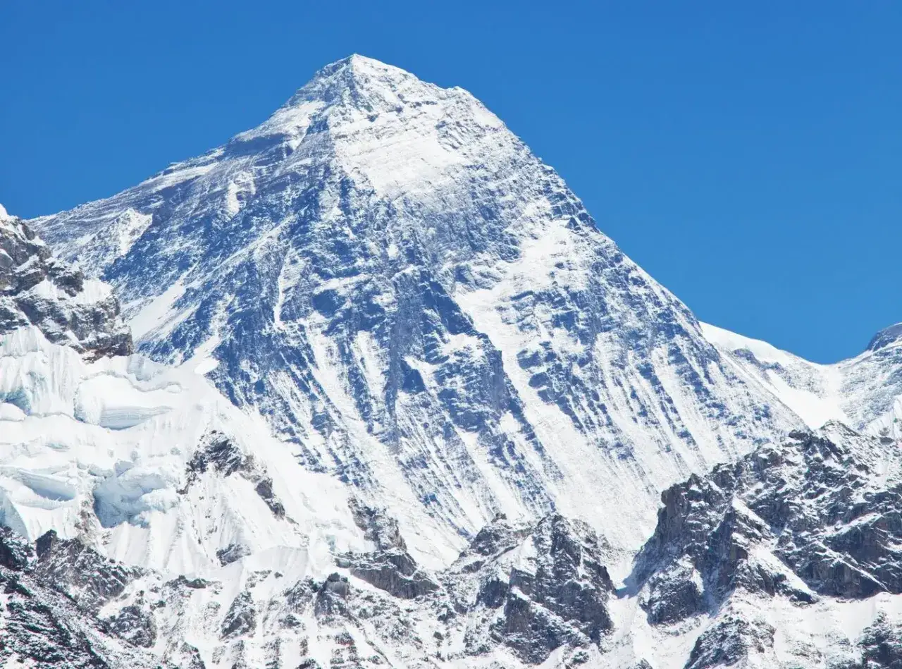 Majestatyczny szczyt Mount Everest, najwyższej g&oacute;ry na świecie, pokryty śniegiem i lodem, g&oacute;ruje na tle błękitnego nieba.