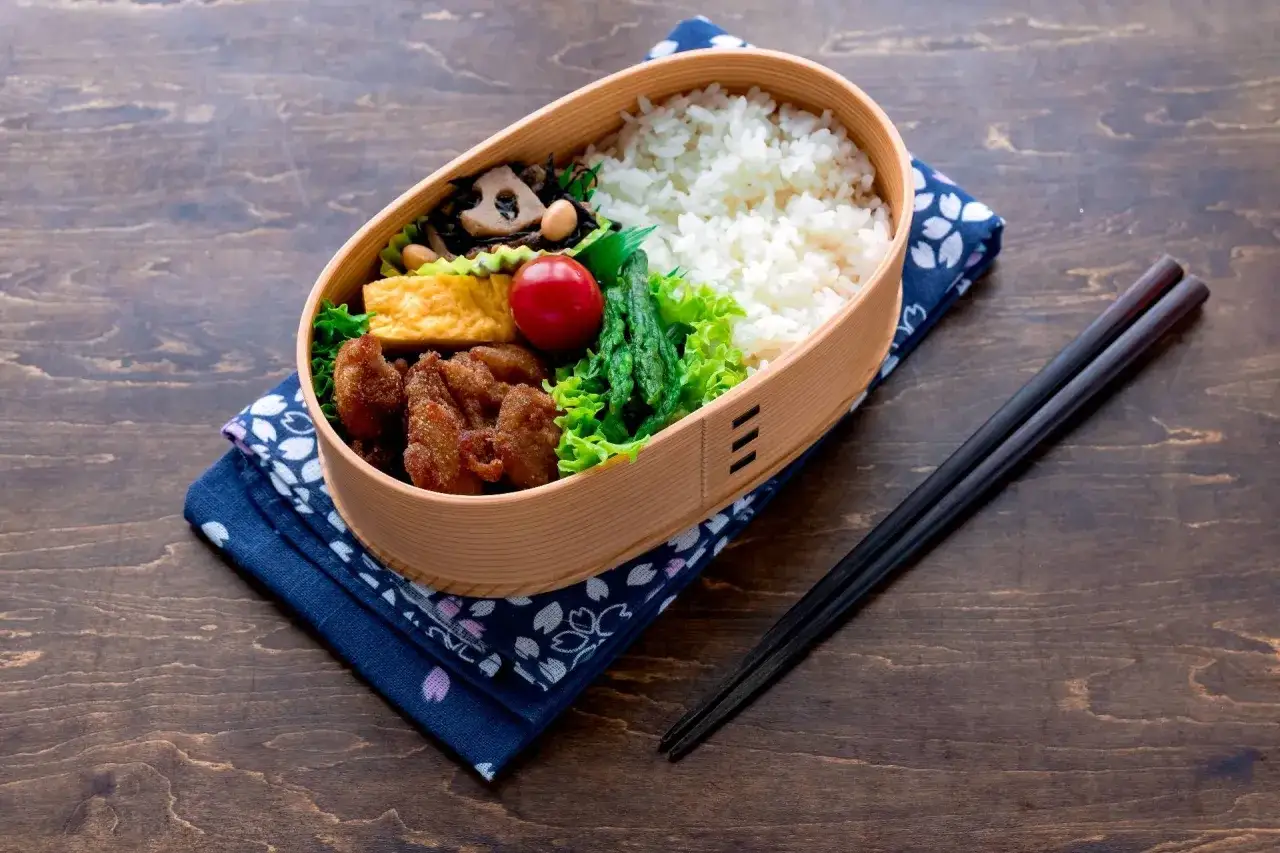 A delicious bento box, a classic of Japanese cuisine, filled with rice, fried chicken, tamagoyaki, and vegetables.