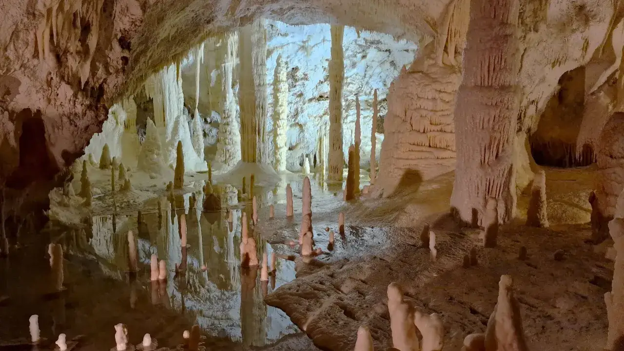 Stalattiti e stalagmiti creano un paesaggio surreale nelle grotte nelle Marche, con riflessi sull'acqua che raddoppiano la magia.