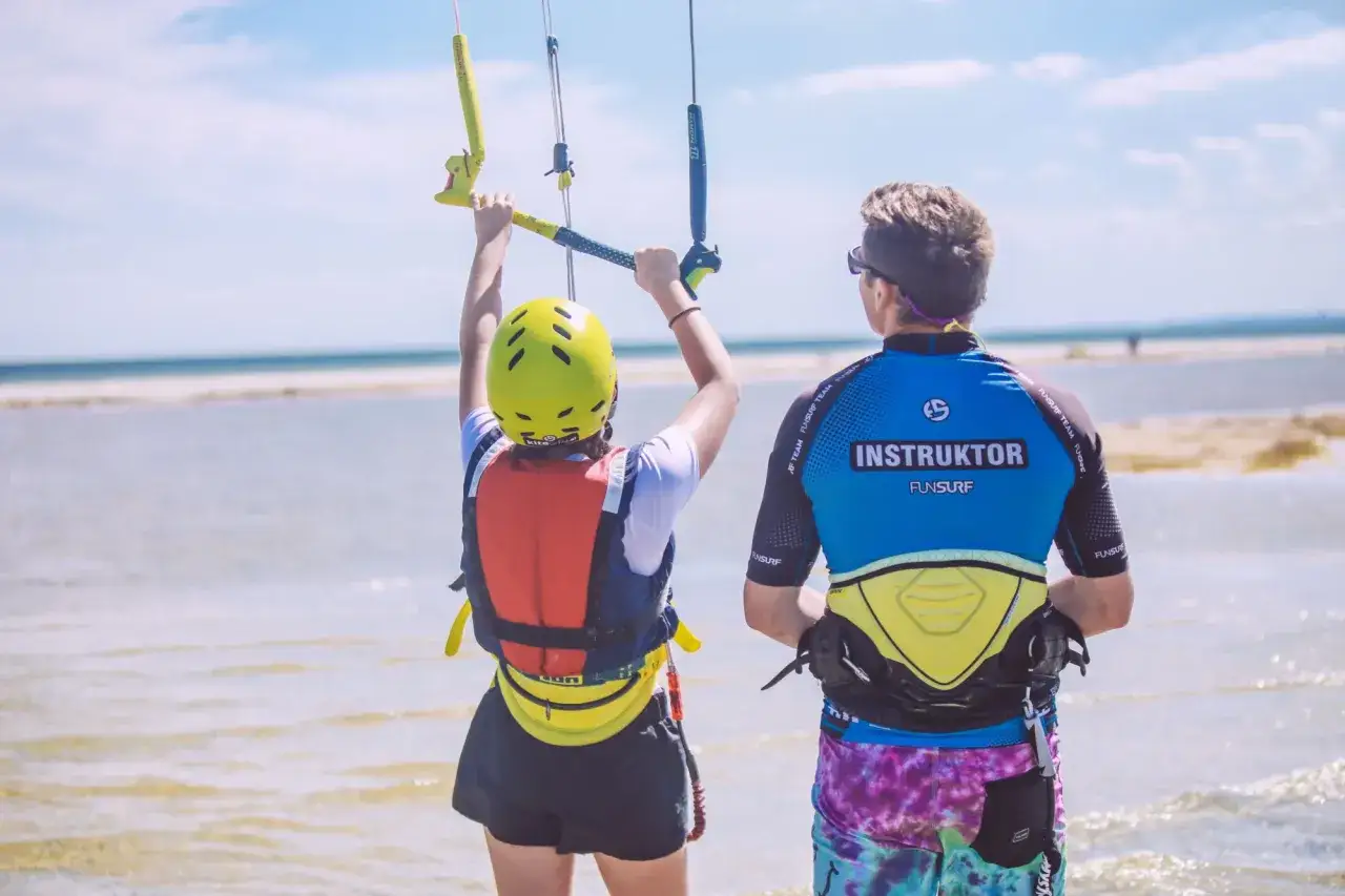 Instruktor kitesurfingu pokazuje, jak trzymać drążek sterowniczy. Nauka kitesurfingu na płytkiej wodzie.